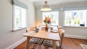 A dining area with a wooden table, chairs, a hanging light fixture, and a window with a view of greenery. - Friesenhaus Käpt'n Hahn, house part 04 (Westerland)