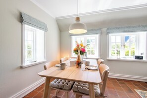 Een eetgedeelte met een houten tafel, stoelen, een hanglamp en een raam met uitzicht op groen.