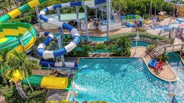 A water park with a large pool, multiple water slides, and a flag. - Spacious 2BR Condo at Harbourside Resort, Walk to Beach (Indian Rocks Beach)
