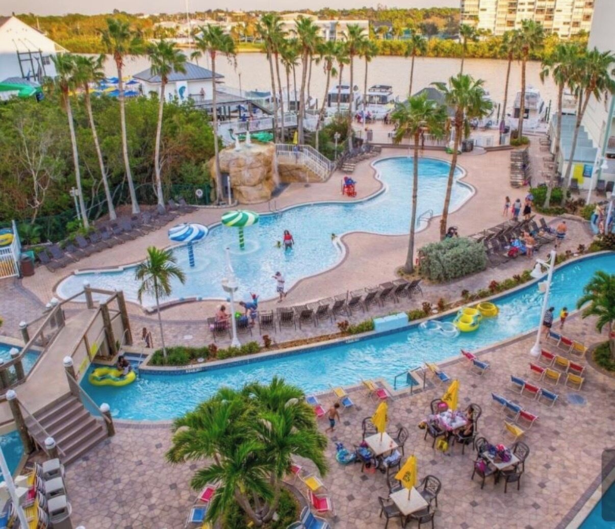 Zona de piscina en un resort con varias piscinas, palmeras y sillones de descanso.