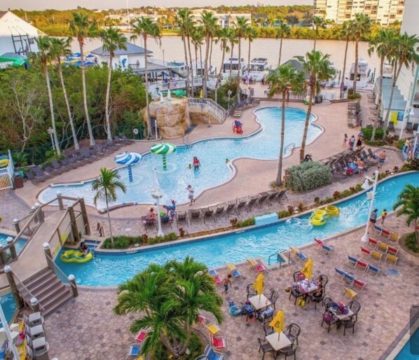 A resort pool area with multiple swimming pools, palm trees, and lounge chairs.