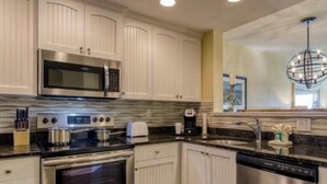 A modern kitchen with white cabinetry, stainless steel appliances, a granite countertop, and a built-in microwave. - Spacious 2BR Condo at Harbourside Resort, Walk to Beach (Indian Rocks Beach)