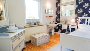 A bedroom with a bed, a bedside table, a nightstand, a window, a radiator, a dresser, and a mirror. - Vacation Rental "LOTTTALEBEN 1" for up to 4 people (non-smoking) (Timmendorfer Strand)