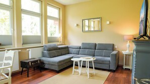 A living room with a sectional sofa, a small table, a white chair, a fireplace, and large windows. - Vacation Rental "LOTTTALEBEN 1" for up to 4 people (non-smoking) (Timmendorfer Strand)