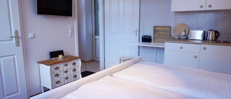 A bedroom with a bed, a TV, a desk with a computer, and a kitchenette.