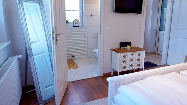 A bedroom with a bed, a dresser, a television, and a bathroom visible through an open door. - Vacation Rental "LOTTALEBEN 2" for up to 2 people (non-smoking) (Timmendorfer Strand)