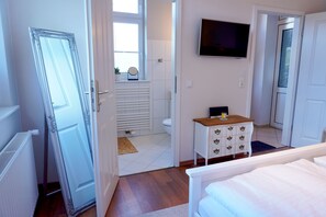 A bedroom with a bed, a dresser, a television, and a bathroom visible through an open door. - Vacation Rental "LOTTALEBEN 2" for up to 2 people (non-smoking) (Timmendorfer Strand)