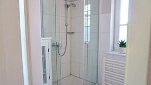 A glass-enclosed shower with a white tiled wall, a window with blinds, and a potted plant on a shelf. - Vacation Rental "LOTTALEBEN 2" for up to 2 people (non-smoking) (Timmendorfer Strand)