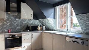Eine moderne Küche mit Backofen, Mikrowelle und Geschirrspüler von Bosch, einem Fenster mit Blick auf ein Backsteingebäude und einem besonderen, geneigten Deckenstil.