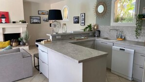 A modern kitchen with a central island, built-in dishwasher, and a dining area with a grey sofa. - Unique Villa Claire de Lune - Jacuzzi - Swimming pool (Sainte-Maxime)