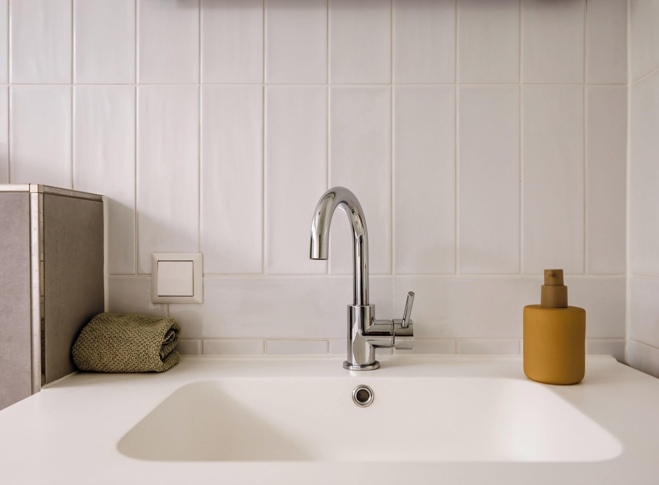 Un baño con lavamanos blanco, grifo cromado y una toalla color beige al lado.