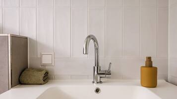 Un baño con lavamanos blanco, grifo cromado y una toalla color beige al lado.