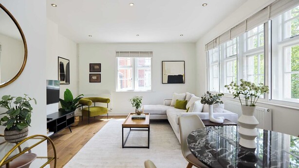 Un salon moderne avec un canapé, une table basse et une table à manger. On y trouve des plantes, un téléviseur et de grandes fenêtres.