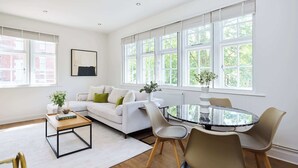 Un salon moderne avec un canapé blanc, une table basse en verre et un coin repas avec des chaises.
