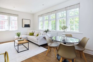 Ein modernes Wohnzimmer mit einem weißen Sofa, einem Glastisch und einem Essbereich mit Stühlen.