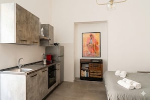 A compact kitchen with a sink, stove, and cabinets, a bed with towels, and a framed artwork on the wall. - Meta CC Palace  (Meta)