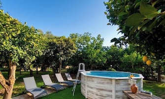 Un patio trasero con un jacuzzi, sillas de descanso y un árbol.