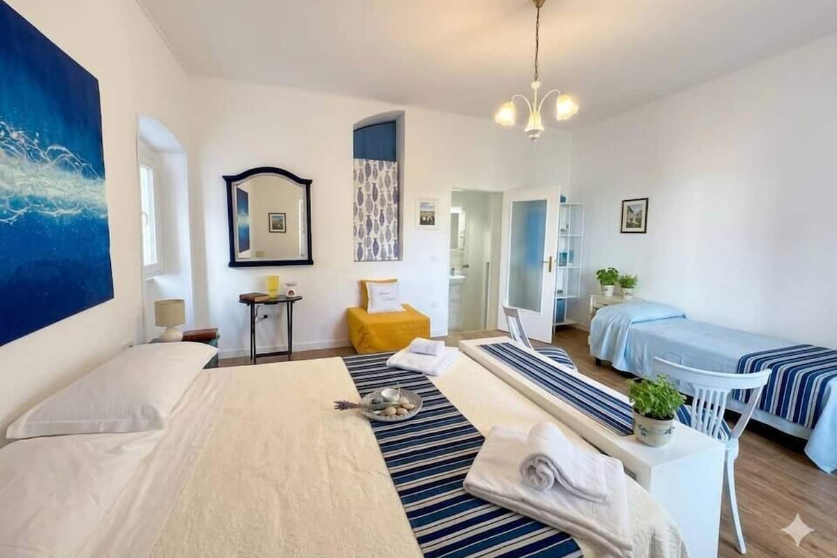 Ett hotellrum med en stor säng, en mindre säng, ett skrivbord med en stol, en spegel, en taklampa och utsikt över korridoren.