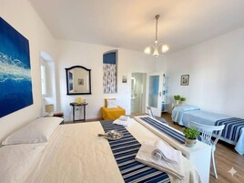 Habitación de hotel con una cama grande, una cama más pequeña, un escritorio con silla, un espejo, una lámpara en el techo y vista al pasillo.