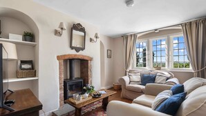 A living room with a fireplace, sofa, and a television. - Alms House West, Grade II Listed, Garden & Patio (Forthampton)