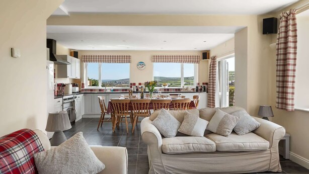 A modern living room with a sofa, a dining table, and a kitchen in the background. - Spacious Home, Private Parking & Garden, Tintagel (Tintagel)