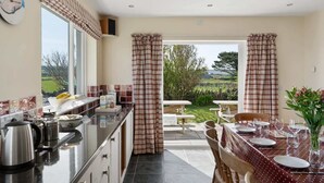 A kitchen with a view to a garden, a dining area with a table set for four, and a window with curtains. - Spacious Home, Private Parking & Garden, Tintagel (Tintagel)