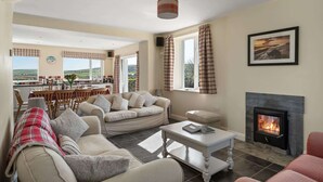 A living room with a sofa, coffee table, fireplace, and a view of the kitchen and outside. - Spacious Home, Private Parking & Garden, Tintagel (Tintagel)