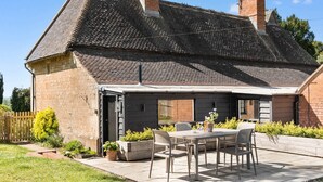 Une maison avec un toit en tuiles, des murs en briques, un patio avec une table et des chaises, et une cour clôturée.