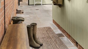 Un couloir avec un banc, des bottes, un porte-manteau et une petite table sur laquelle est posée une plante.