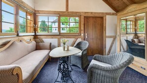 Una stanza con soffitto in legno, ampie finestre, un divano, un tavolo e poltrone in vimini.