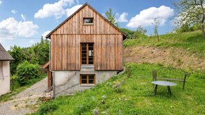 Una casa di legno con tetto spiovente, un piccolo portico e una panchina nel giardino.