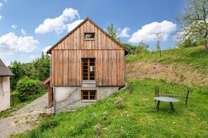 Une maison en bois avec un toit en pente, un petit porche et un banc dans la cour.