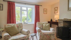 A cozy room with two floral armchairs, a small round table, a fireplace, and a window with curtains. - Harbins Farm (Sherborne)