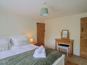 A bedroom with a bed, a bedside table with a lamp, a wooden dresser, and a door. - Harbins Farm (Sherborne)