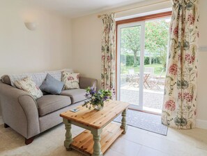 A living room with a sofa, a wooden coffee table, and a view of an outdoor patio with chairs. - Harbins Farm (Sherborne)