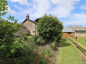 A stone house with a chimney, surrounded by a fenced yard and a large bush. - Harbins Farm (Sherborne)