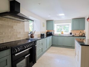 A modern kitchen with a black stove, light green cabinets, and a window providing natural light. - Harbins Farm (Sherborne)