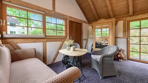 A cozy room with wooden beams, a round table with chairs, and large windows.