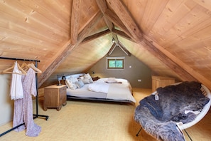 Ein gemütliches Schlafzimmer im Dachgeschoss mit schrägem Dach, einem Bett, einem Sessel und einem Fenster.
