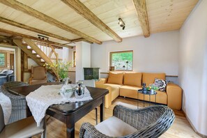 Ein gemütliches Wohnzimmer mit Holzboden, einer Couch, einem Tisch mit Spitze und Korbstühlen sowie einer Treppe.