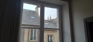Ein Zimmer mit einem großen Fenster, einer Tür und Blick auf ein Gebäude mit Ziegeldach und zwei Türmen.