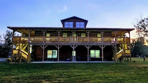 A two-story building with a central tower, multiple balconies, and a grassy field in front.