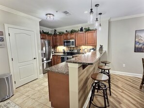 A kitchen with wooden cabinets, stainless steel appliances, a granite countertop, and a bar area with stools. - UPDATED Downtown Gatlinburg on the strip, Heated Pool, Hot tub (Gatlinburg)