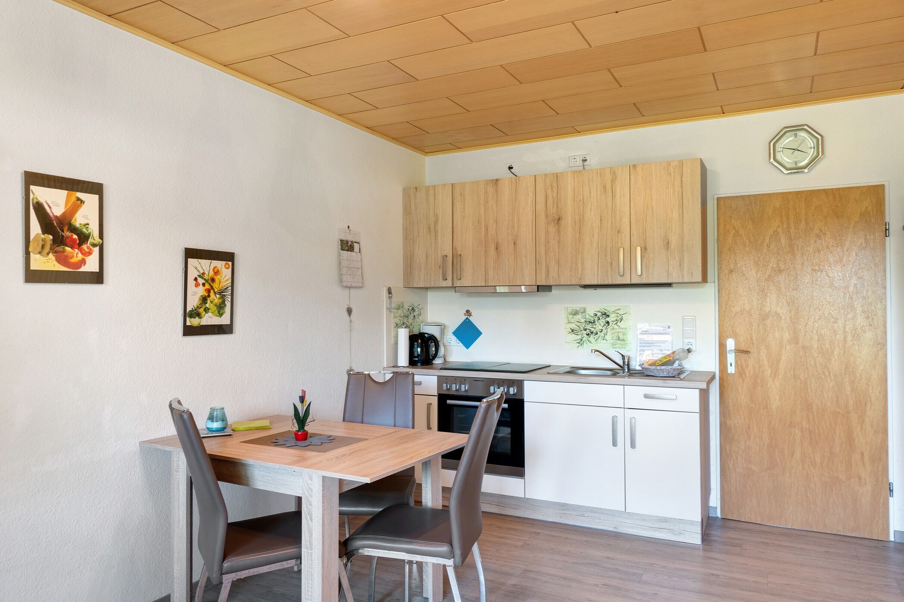 A compact kitchen with wooden cabinets, a built-in oven, and a dining area with a table and chairs.