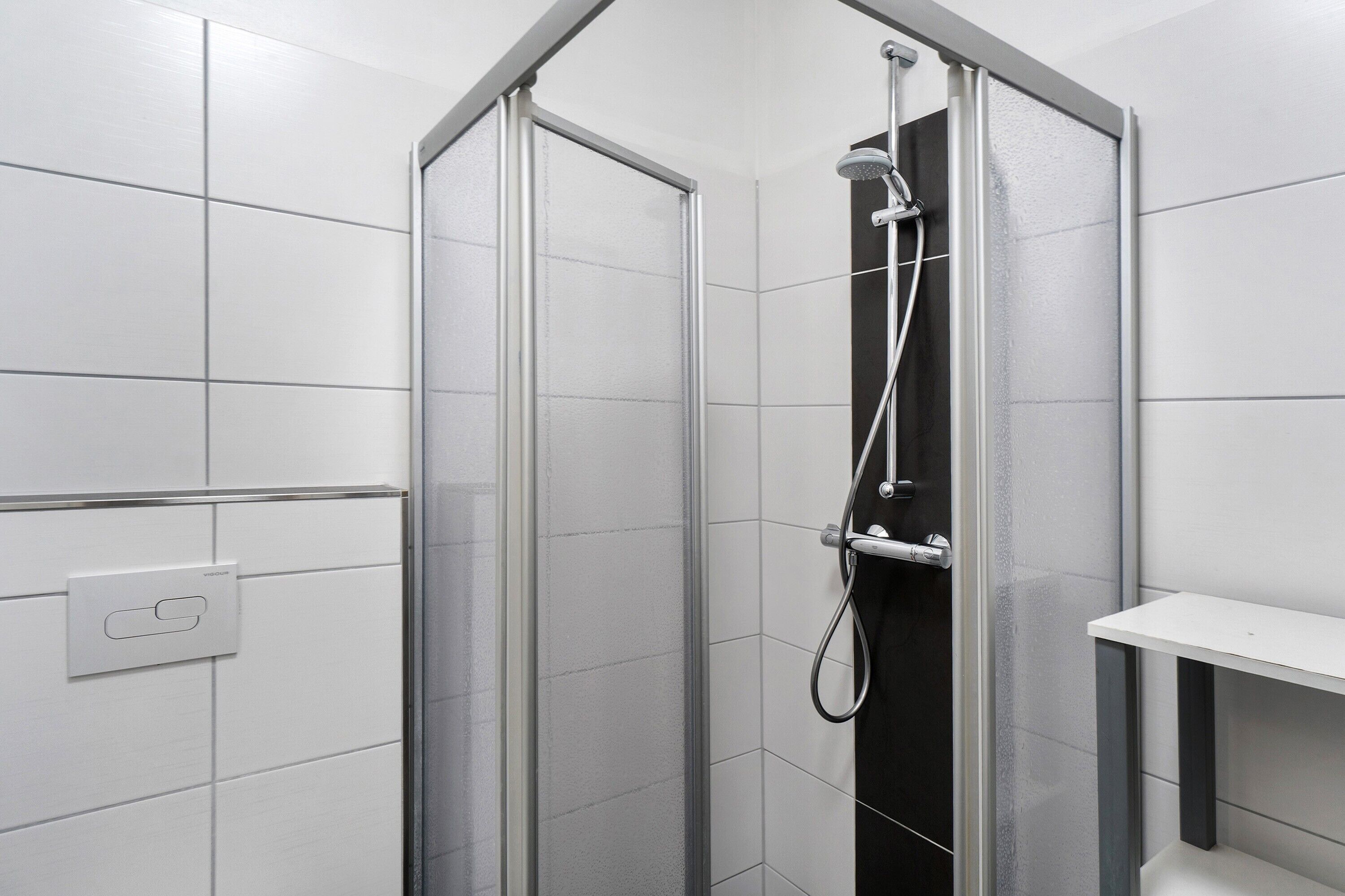 Eine Dusche mit Glastür, Duschkopf zum Handgebrauch und einer fest montierten Bedienkonsole.