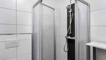 Eine Dusche mit Glastür, Duschkopf zum Handgebrauch und einer fest montierten Bedienkonsole.