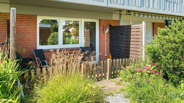 A residential property with a balcony, a brick wall, a wooden fence, and a garden with various plants and flowers. - Apartment 'In The House Juist' with Private Terrace and Wi-Fi (Dornum)