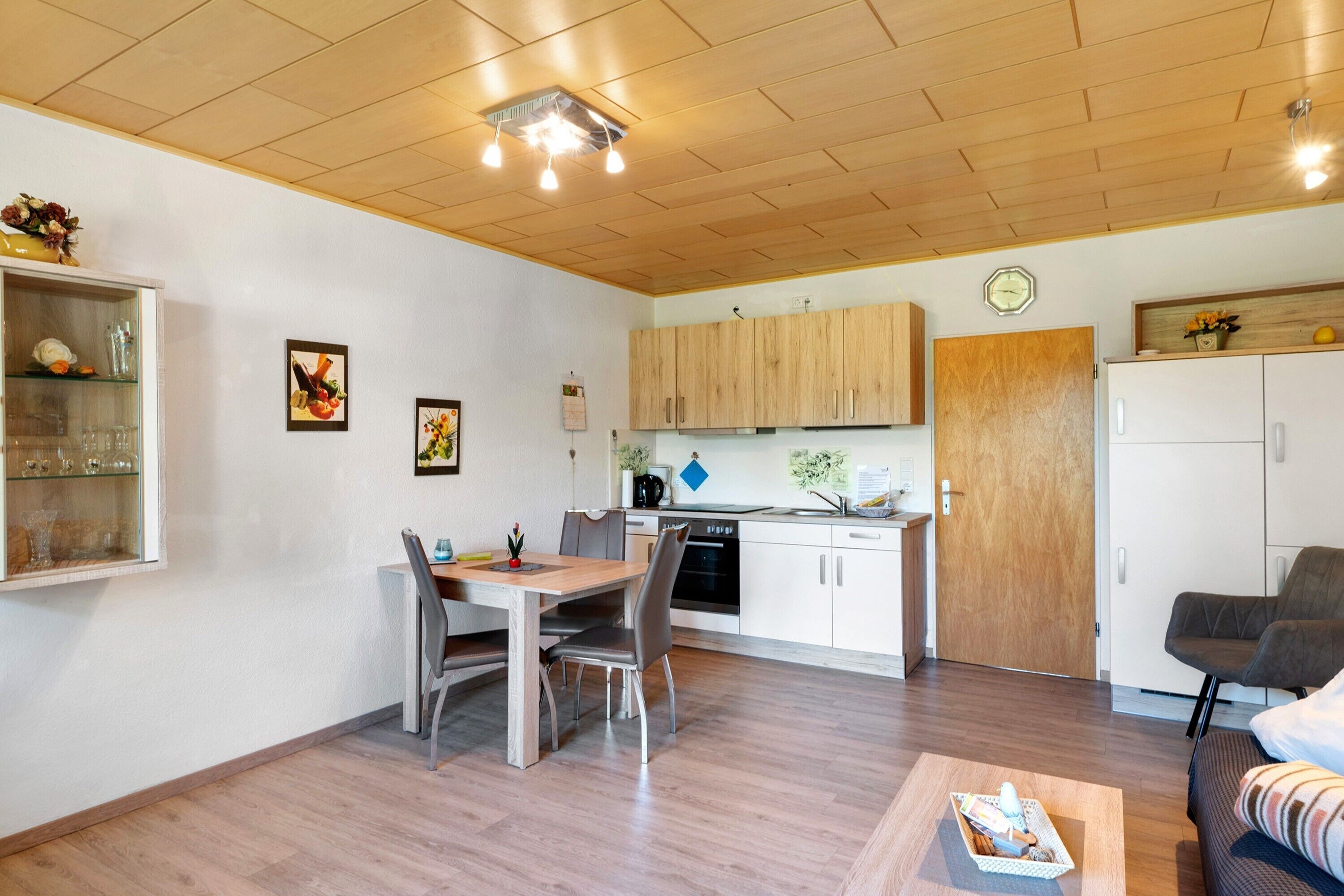 Een compacte keuken met houten kastjes, een eethoek met een tafel en stoelen, en een woongedeelte met een bank en salontafel.