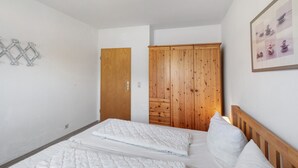 A bedroom with a bed, a wooden wardrobe, and a wall-mounted light fixture. - Apartment 'In The House Juist' with Private Terrace and Wi-Fi (Dornum)
