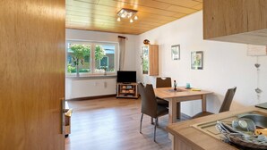 A modern kitchen with wooden cabinetry, a dining table with chairs, and a view of the outdoors through large windows. - Apartment 'In The House Juist' with Private Terrace and Wi-Fi (Dornum)